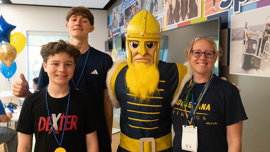 A women and two boys pose with a mascot of Gus the Viking