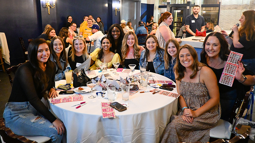 Several young alumni gather around a table while playing bingo