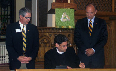 Augustana of Sioux Falls President Rob Oliver, left, and Augustana of Rock Island President Steve Bahls look on as the Rev. Mark Wilhelm of the ELCA signs a compact in recognition of the 150th anniversary of the Augustana Synod.