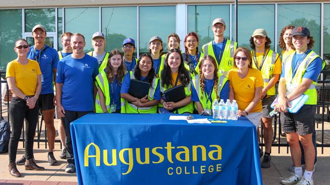 Students and faculty posing in front of an Augustana College table