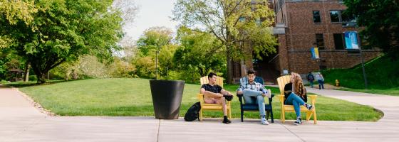 Three students sitting in chairs in the Viking Plaza with the Gerber center brown building behind them.